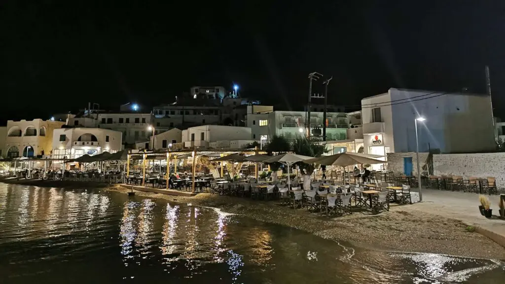 Experience the enchanting beauty of Kythnos Island with a nighttime view of its seaside town. Outdoor restaurants line the shoreline, their ambiance enhanced by the glow of streetlights and building lights, making it a perfect travel destination for any eager guide.