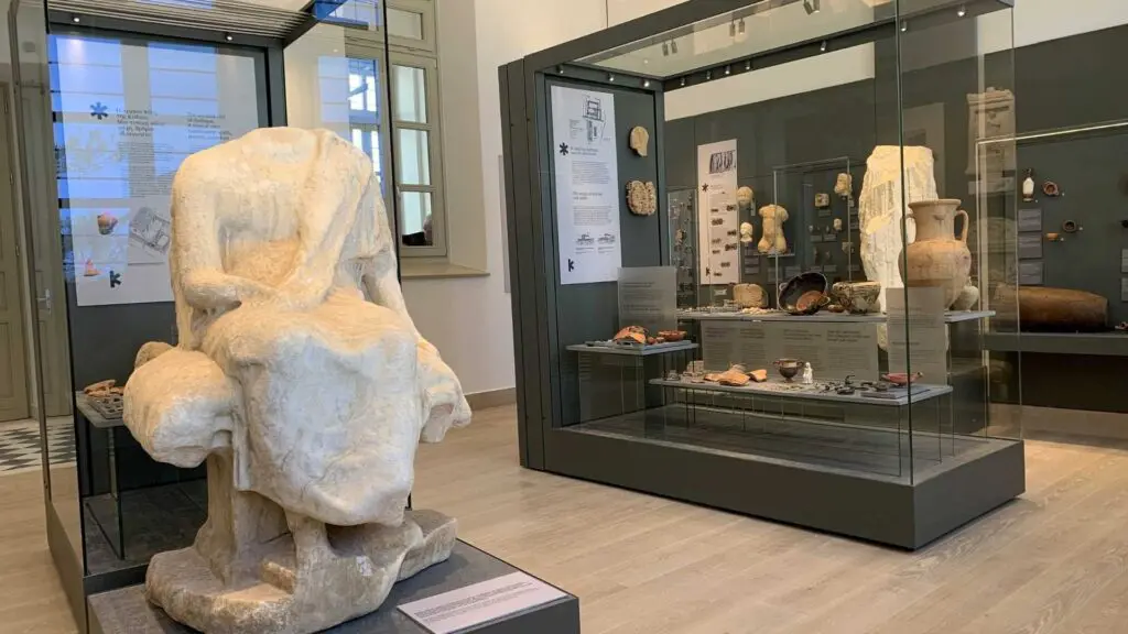 Explore the captivating museum exhibit featuring ancient artifacts from Kythnos Island, including a headless marble statue. Glass cases display pottery and tools, while information panels provide historical context, making it a perfect stop on your travel guide through history.