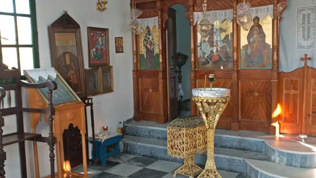 An interior of a small chapel on the island of Kythnos features religious icons on the walls, a gold baptismal font, and wooden paneling—a hidden gem in any travel guide.
