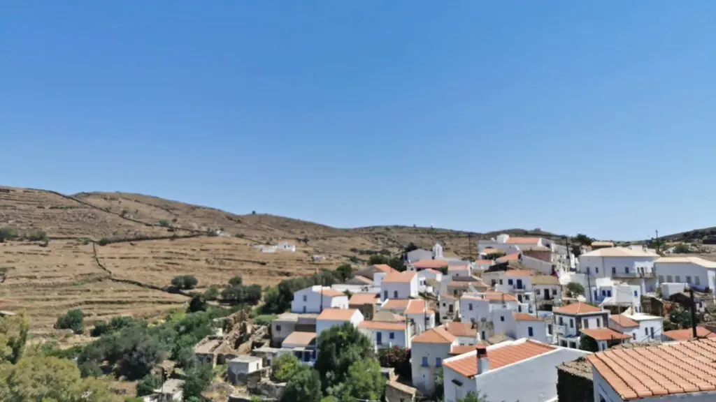 Discover the charm of a hillside village on Kythnos Island, where white houses with red roofs dot the terraced terrain beneath a clear blue sky. Your perfect travel guide to serene beauty awaits.