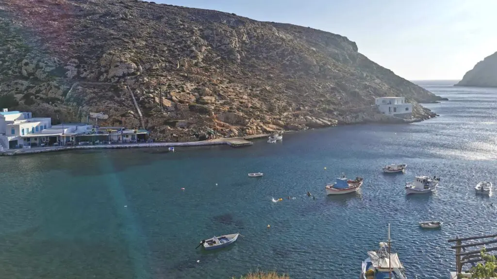 Heronissos bay on the island of Sifnos, with rocky hills, several small boats in the water, and a few white buildings along the shoreline. This gem is a must-see in any travel guide exploring the beauty of Greek islands.