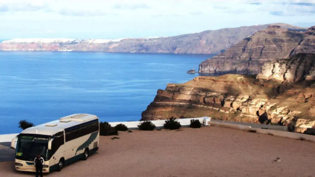 A tour bus parked above Santorini's ferry port offers a breathtaking view of the ocean and rugged coastline, capturing the island's natural beauty.