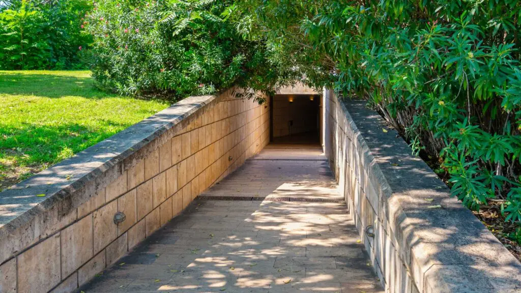 A stone pathway gracefully weaves its way through lush green bushes and grass, leading to the enchanting underground passage of Vergina.