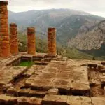 Ancient stone ruins and columns grace a mountainous landscape, evoking the mystique of once-vibrant royal sites. The hills and cloudy sky in the background whisper secrets of past oracles and gods, leaving an air of timeless wonder.
