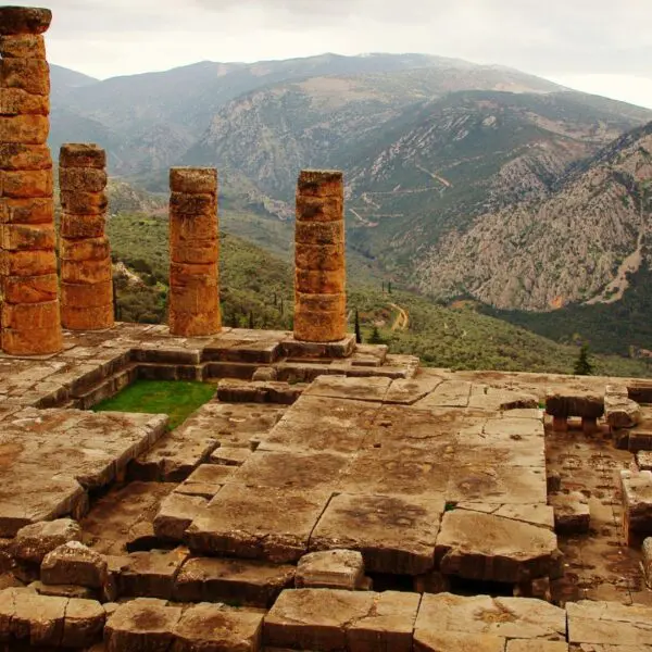 Ancient stone ruins and columns grace a mountainous landscape, evoking the mystique of once-vibrant royal sites. The hills and cloudy sky in the background whisper secrets of past oracles and gods, leaving an air of timeless wonder.