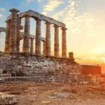 The ancient stone columns of the Temple of Poseidon at Cape Sounion, Greece, stand against a sunset sky with the sea and a distant island in the background—one of the must-see places to visit in Greece. The ancient stone columns of the Temple of Poseidon at Cape Sounion, Greece, stand against a sunset sky with the sea and a distant island in the background—one of the must-see places to visit in Greece.