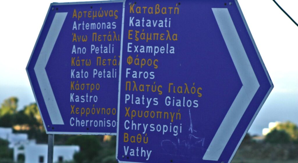 A bilingual road sign on Sifnos Island displays directions in Greek and English, guiding travelers to locations such as Artemonas, Katavati, and Faros, among others. Perfect for anyone using a travel guide to explore the island's charming destinations.