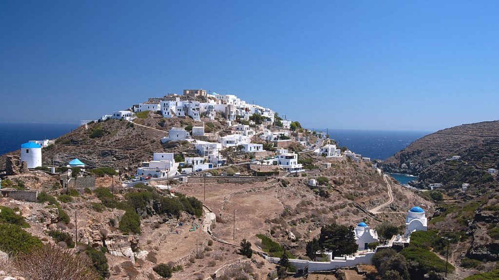 Kastro, Sifnos Island - Perched on a hillside, Sifnos Island's charming village features white buildings and blue domes that overlook the tranquil sea under a clear blue sky, creating an idyllic travel destination for any guidebook.