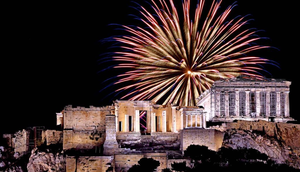 Fireworks burst above the illuminated Parthenon on the Acropolis in Athens at night, creating a magical scene that's perfect for those exploring things to do during an unforgettable Athens Christmas.