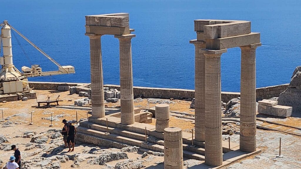 Ancient Greek ruins with tall stone columns overlook the sea on a sunny day, as travelers on Greek island-hopping itineraries explore the historic site.