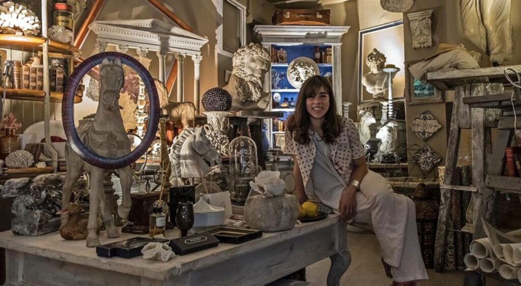 In a cluttered room brimming with sculptures, art pieces, and various objects, a woman finds inspiration. Whether exploring things to do in Athens or planning an Athens Christmas getaway, creativity thrives amid the chaos.