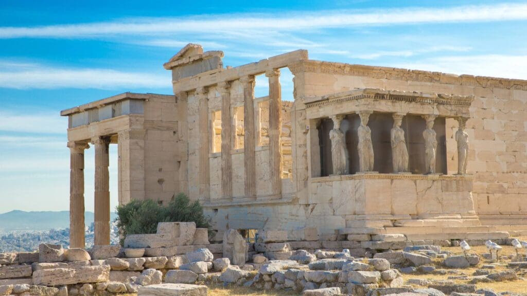 Explore the ancient Greek temple ruins with majestic stone columns and statues under a blue sky, nestled in rocky terrain. Embark on an acropolis self-guided tour to fully experience this historical marvel at your own pace.