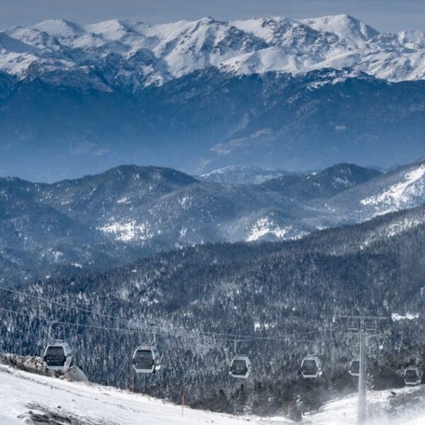 Snow-covered mountains with a ski lift in the foreground stretch across a winter landscape under a cloudy sky, reminiscent of the stunning Greek ski resorts.