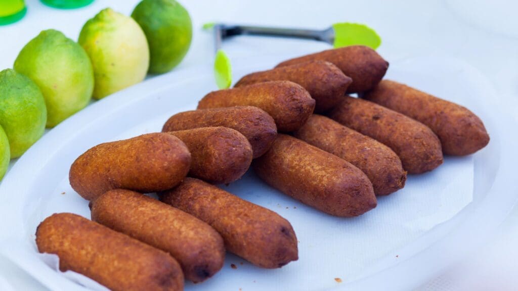 A plate of fried croquettes, reminiscent of Greek street food delights, is arranged neatly with limes in the background.