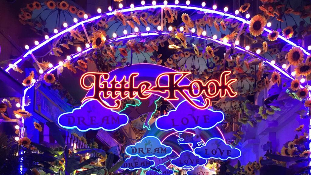 The vibrant neon sign for "Little Kook" in Athens, adorned with sunflowers, reads "Dream" and "Love" in a colorful, illuminated display. A must-see spot among things to do in Athens, it transforms into a festive wonderland during the enchanting Athens Christmas season.