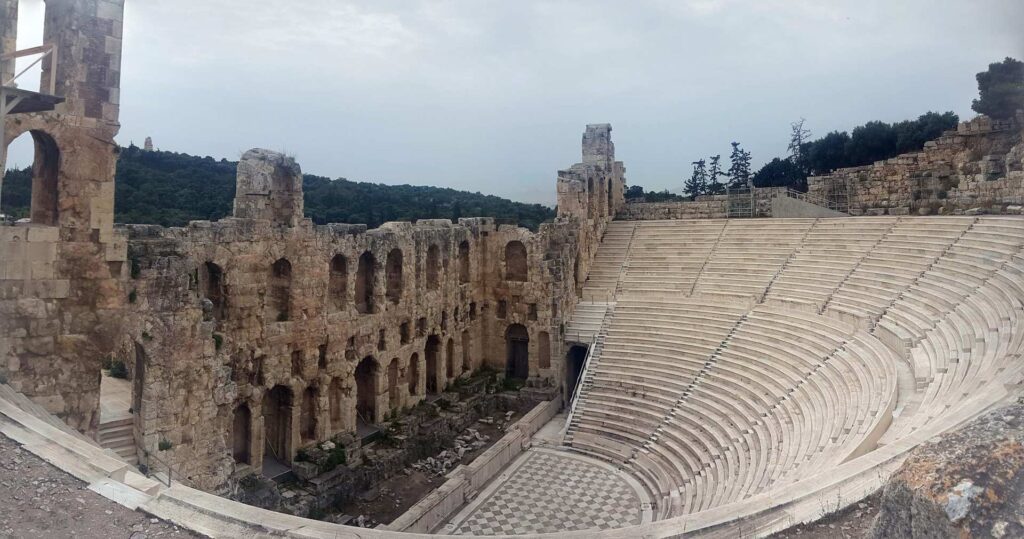 Explore this ancient amphitheater with stone ruins and tiered seating under a cloudy sky, surrounded by trees. Offering historical insights, it's like an insider's guide to the past—a gem tucked away, reminiscent of the majestic Acropolis.