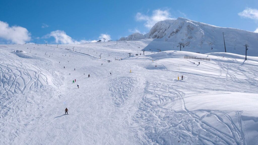 People are skiing and snowboarding on a wide, snowy mountain slope under a clear blue sky, enjoying the festive spirit as Christmas approaches.