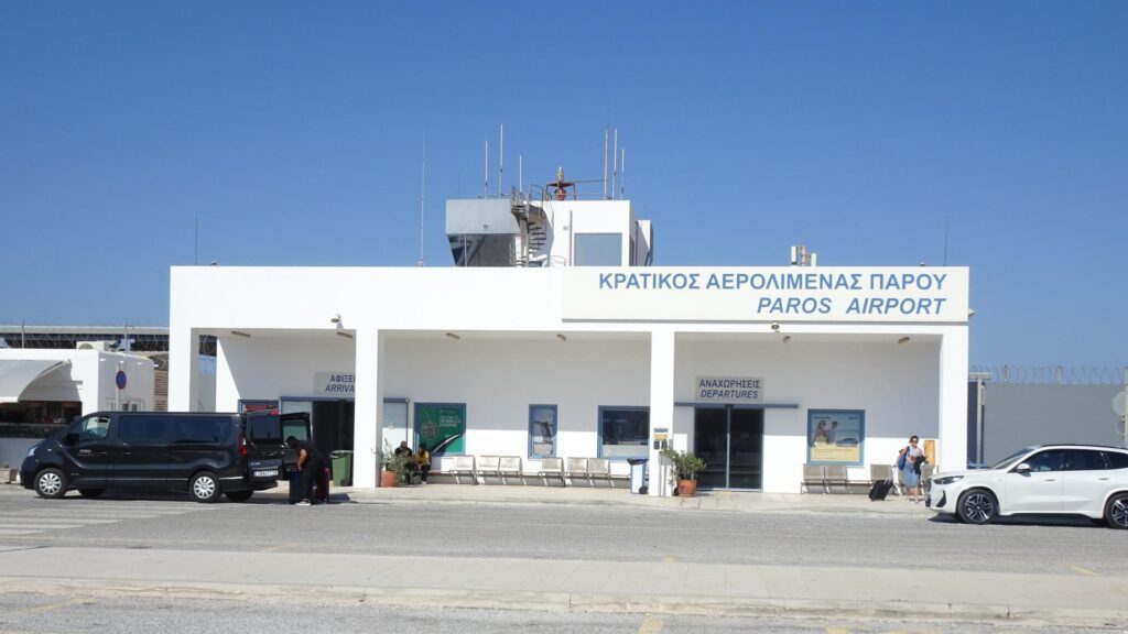 Front view of Paros Airport building with people and vehicles bustling outside, under a clear blue sky—a vibrant scene for any Island Guide exploring the beautiful Cyclades.
