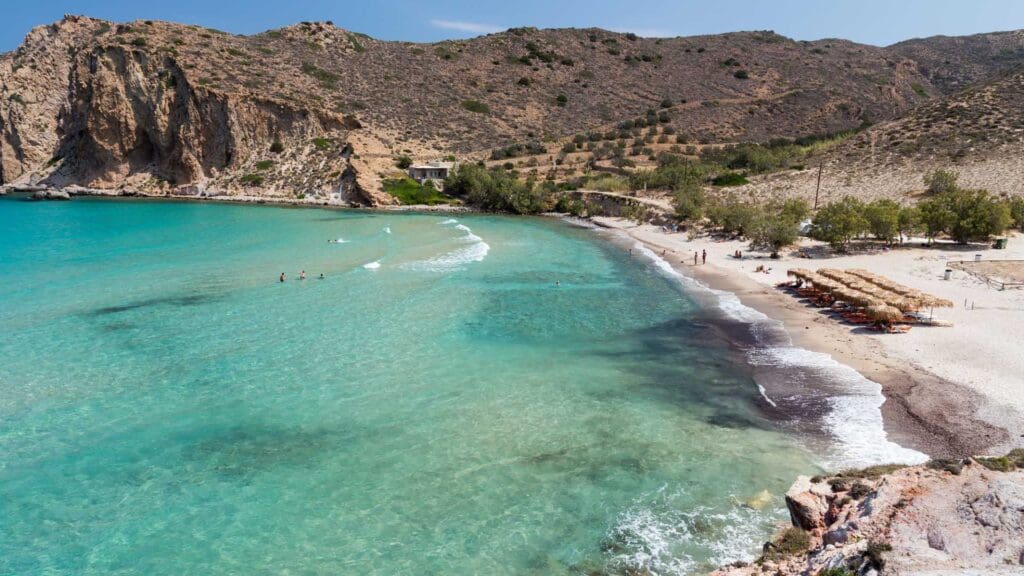 The scenic Milos beaches boast turquoise water, rocky cliffs, and sunbathers on loungers under umbrellas, all surrounded by lush vegetation. These must-see spots capture the essence of paradise.