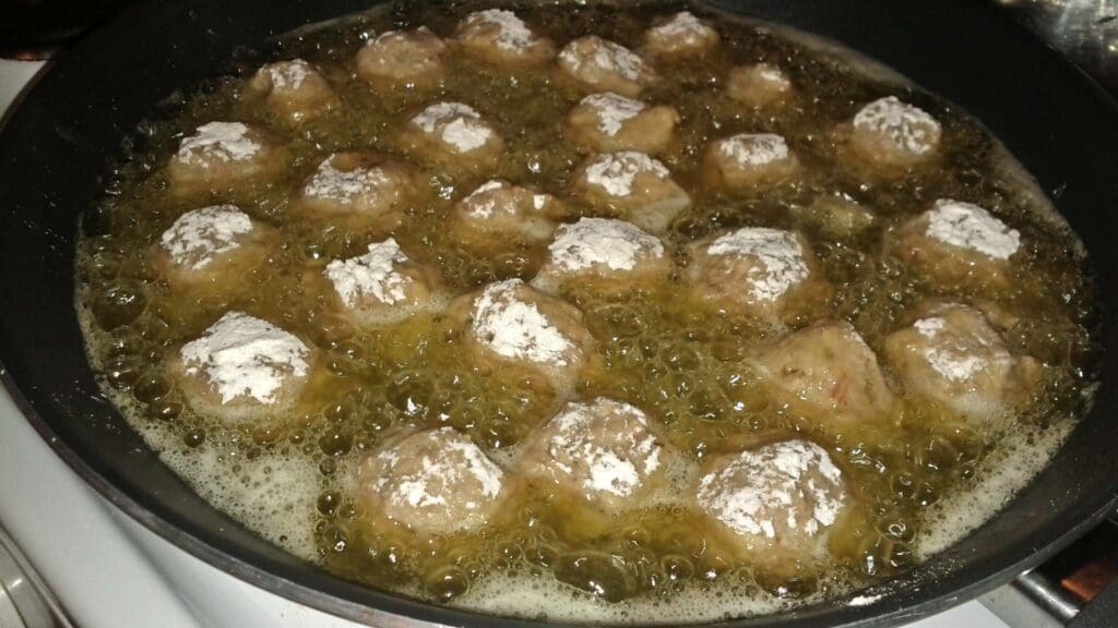 Greek street food comes to life as meatballs sizzle in hot oil, with a delicate dusting of flour on top.