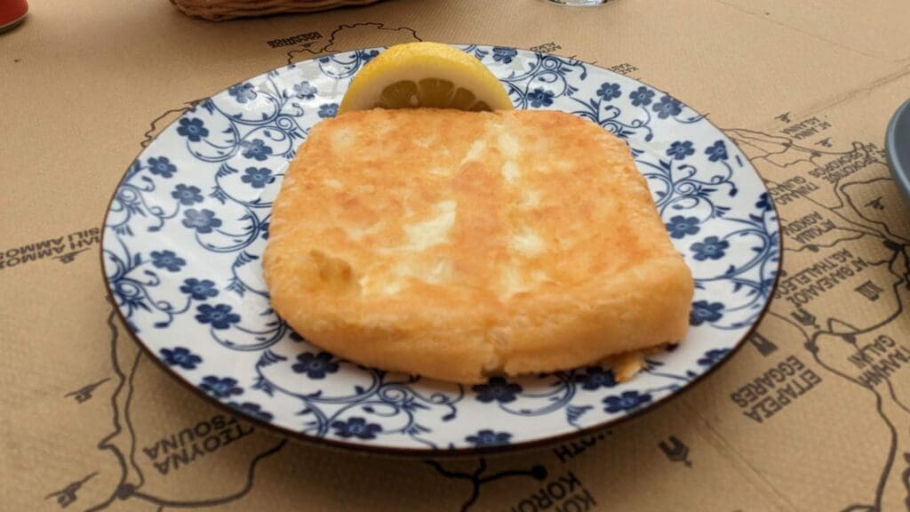 A plate featuring a piece of fried cheese and a lemon wedge on a decorative floral-patterned dish evokes the vibrant flavors of Greek street food.