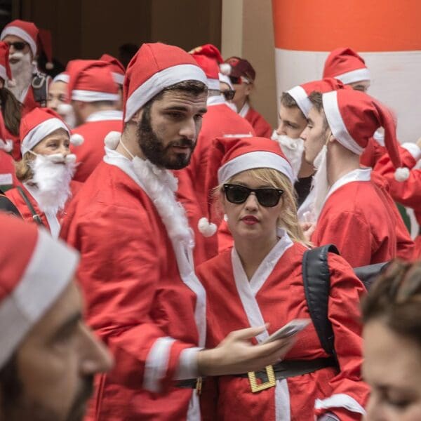 A cheerful crowd of people dressed in Santa costumes gathers outdoors in Athens, many holding smartphones. It’s one of the lively things to do during the Christmas season!