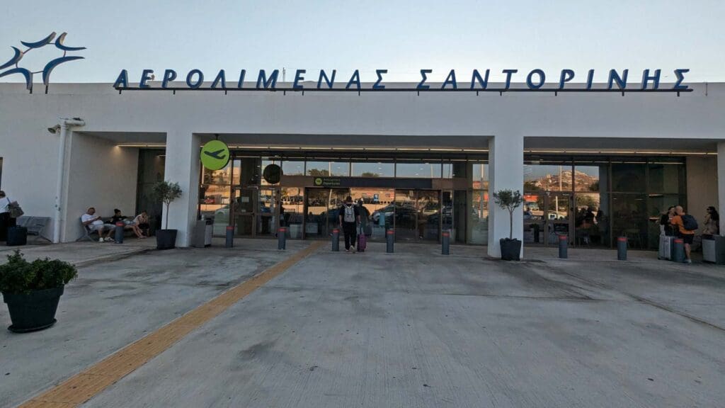 Outside the entrance of Santorini Airport, where people sit and stroll, the welcoming sign in Greek hints at the wonders beyond. Among these destinations is Sikinos Island, waiting to offer its serene beauty and charm.