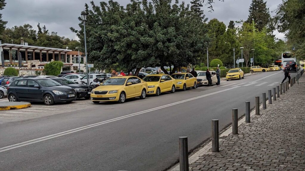 A line of yellow taxis is parked alongside a street, with a few people standing nearby, perhaps sharing historical insights about the area. In the background, trees and a building peek into view, framing this insider's guide to the vibrant neighborhood.