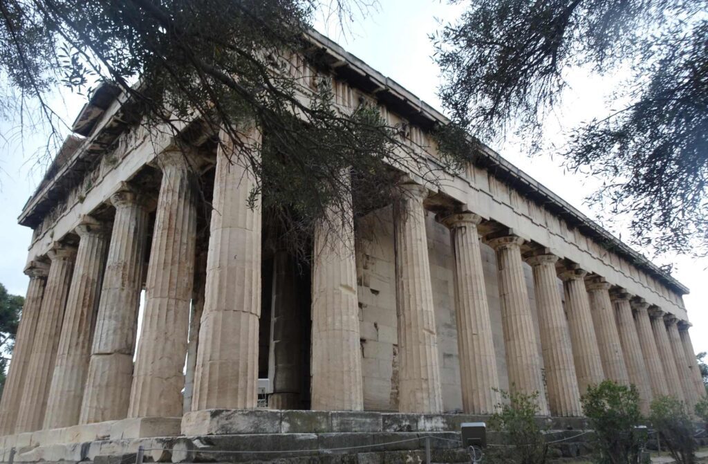Nestled under a cloudy sky, this ancient Greek temple with striking Doric columns stands majestically, partially surrounded by trees. This historic site invites you to ponder how many days in Athens are needed to truly explore its timeless beauty and rich heritage.