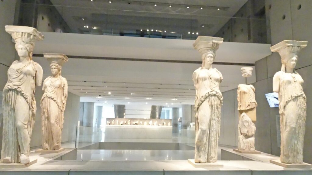 Ancient Greek statues of women, used as columns, known as Caryatids, grace the museum hall with their elegance, surrounded by additional artifacts in the backdrop. As you ponder how many days in Athens would suffice to explore such history, each artifact tells its timeless tale.