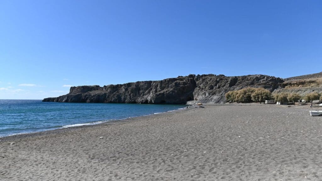 A sandy beach with a rocky cliff in the background and a clear blue sky, reminiscent of the stunning Heraklion beaches.