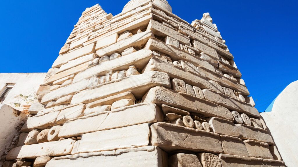A stone structure with an ornate brickwork pattern stands proudly under the clear blue sky, reminiscent of the charming architecture found in Paros.