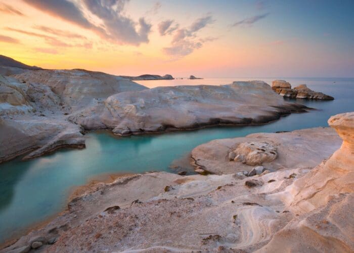 Sarakiniko Beach, Milos Island, Greece -Discover the stunning rocky coastal landscape of Milos at Sarakiniko Beach, where smooth white formations meet turquoise waters under a partly cloudy sunset sky. Perfect for any visitor's guide, this breathtaking view is a must-see for nature lovers and photographers alike.
