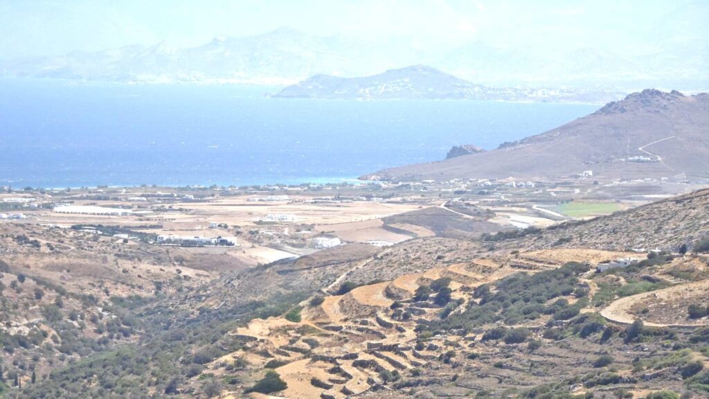 View of the terraced hills of Lefkes, Paros, with the sparkling sea and distant mountains in the background under a clear sky.