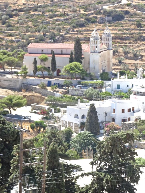 Nestled on a hillside, the picturesque village of Lefkes in Paros, Greece, offers a stunning view of its church with two bell towers, surrounded by lush trees and charming white buildings.