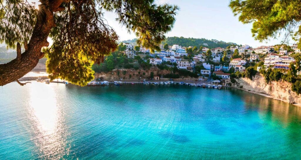 Nestled among small Greek islands, this scenic seaside village features iconic white and blue buildings perched on a hillside, offering breathtaking views of a clear turquoise bay fringed with lush trees.