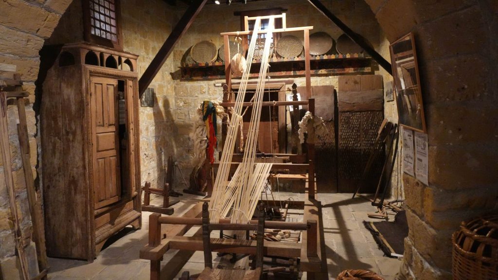 Traditional weaving loom and tools set up in a rustic stone-walled room with wooden furniture and woven baskets—a glimpse into local crafts, perfect for those seeking what things to do in Nicosia Cyprus - Folk Art Museum, Nicosia, Cyprus