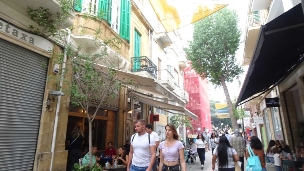 A bustling narrow street in Nicosia, Cyprus, lined with cafes and shops. People stroll and relax outside under vibrant shades and leafy trees, while charming buildings with balconies add to the allure of this enchanting travel guide destination.