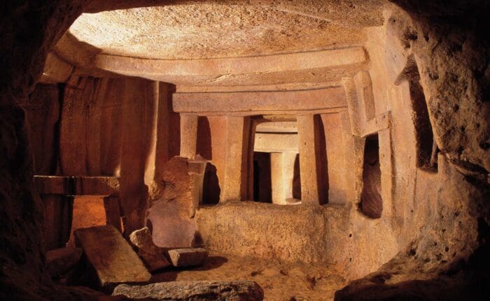 Ancient stone chamber with upright pillars and large slabs, lit by warm light, showing weathered surfaces and rough floor—a remarkable site among the must-see places to visit in Cyprus.