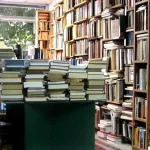 A room filled with tall bookshelves and stacks of books on tables at Moufflon Bookshop, Cyprus